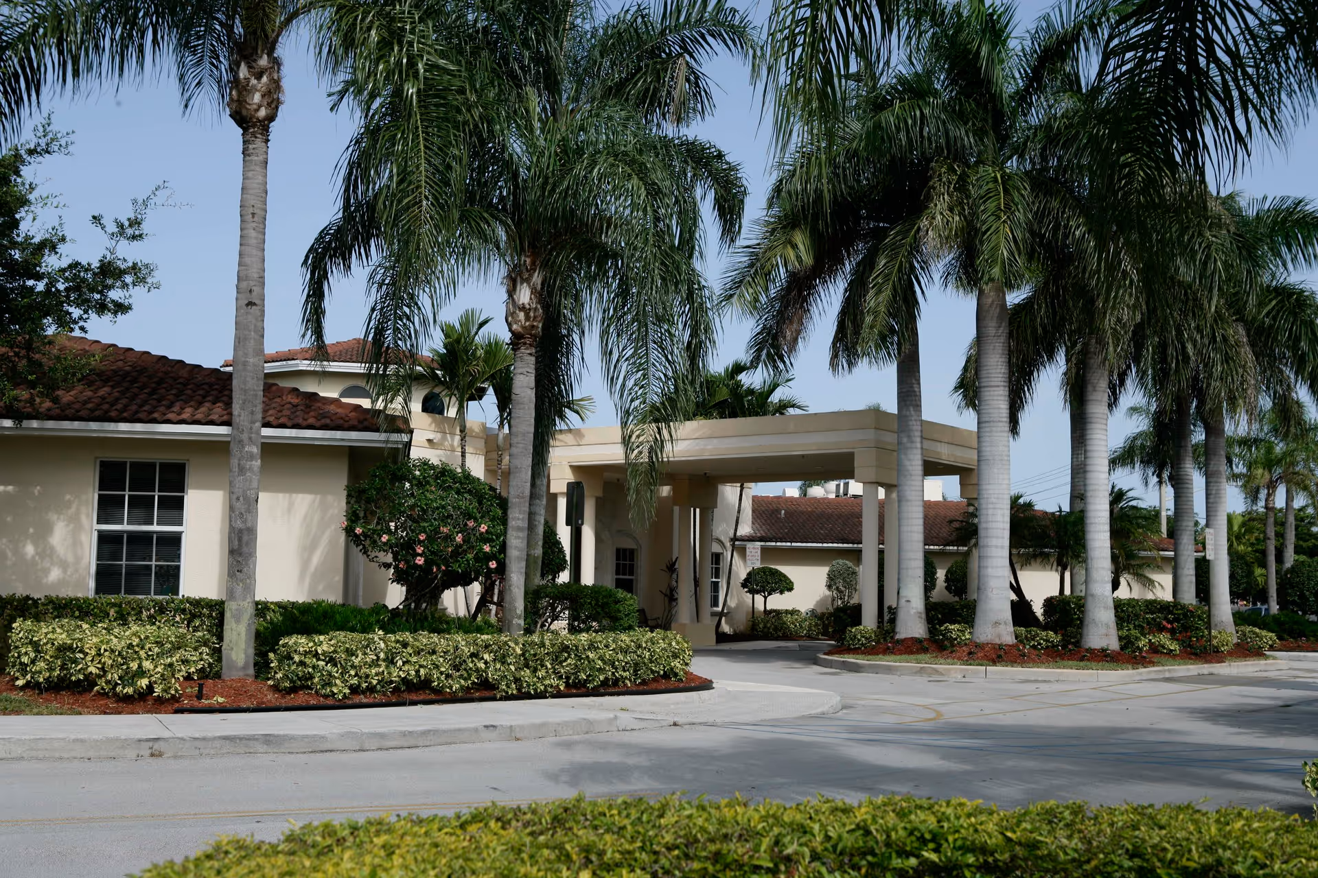 Entrance of HarborChase of Tamarac with a porte-cochere, palm trees and landscaped driveway.
