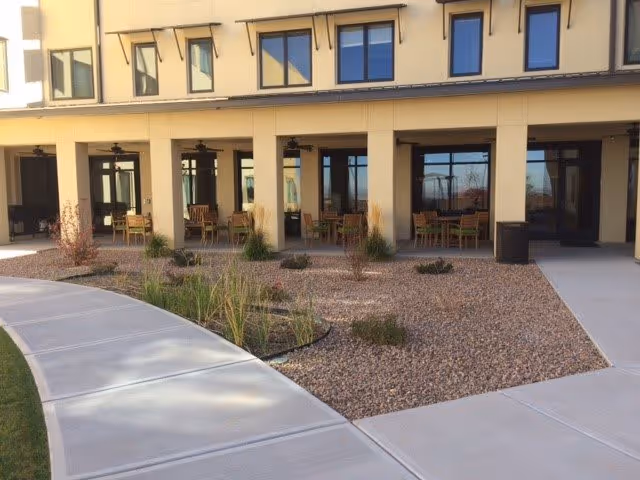 Walkway leading to a landscaped courtyard and covered patio seating along the front of a multi-story building.