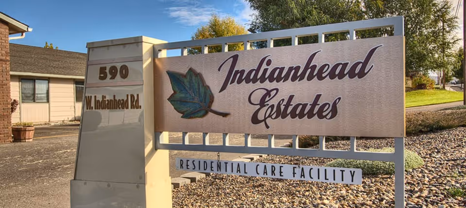 Outdoor sign for Indianhead Estates Residential Care Facility with address 590 W. Indianhead Rd., surrounded by landscaping and a building in the background.