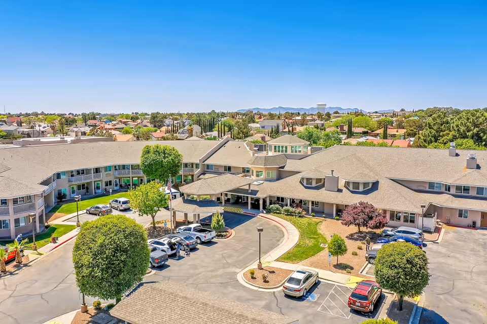 Aerial view of Solstice Senior Living at Rio Norte facility showing a large, two-story building with a circular driveway entrance, surrounded by trees, parked cars, and landscaped grounds under a clear blue sky.