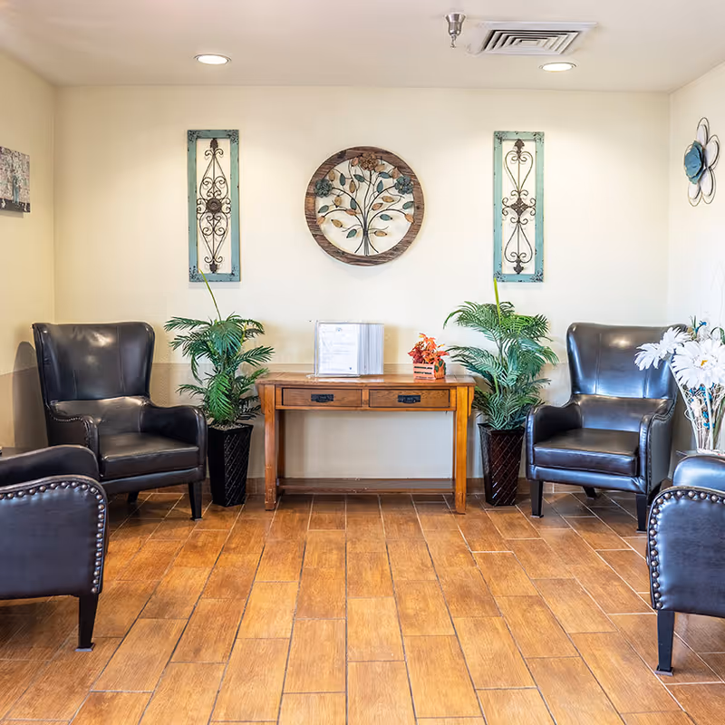 Reception-style seating area with two black leather armchairs flanking a wooden console table, decorative wall art, and potted plants.