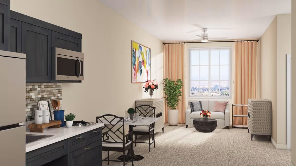 Open-plan living room with a small kitchen area, dining table, sofa by a window, artwork, and plants.