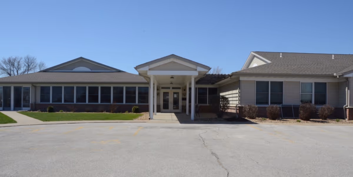 Front entrance of a single-story senior living building with a covered porte-cochère and rows of windows.