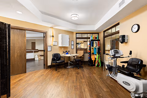 A bright multipurpose interior room with exercise equipment, seating, and therapy supplies.