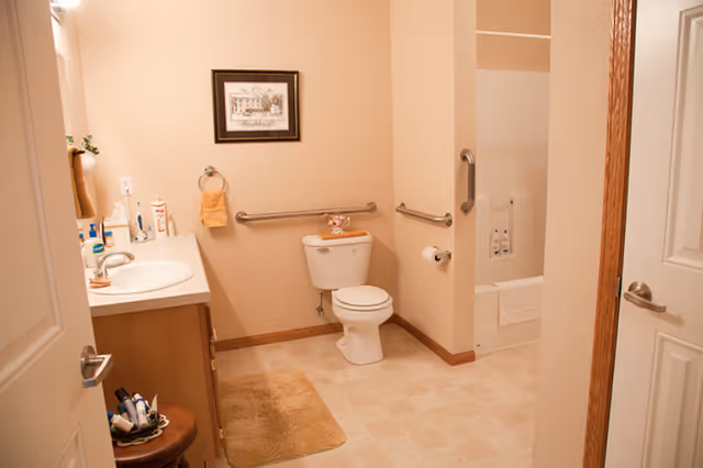 Well-lit accessible bathroom with a toilet, sink vanity, grab bars, and a bathtub/shower.