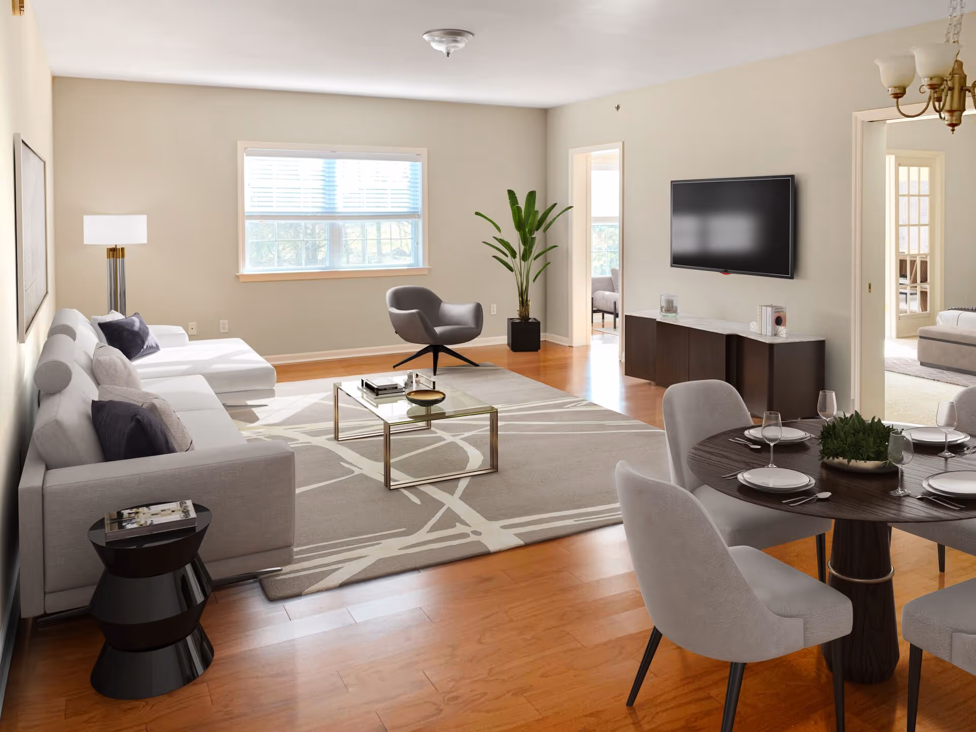 Open-plan living and dining room with a sectional sofa, coffee table, wall-mounted TV, and dining table on hardwood floors.