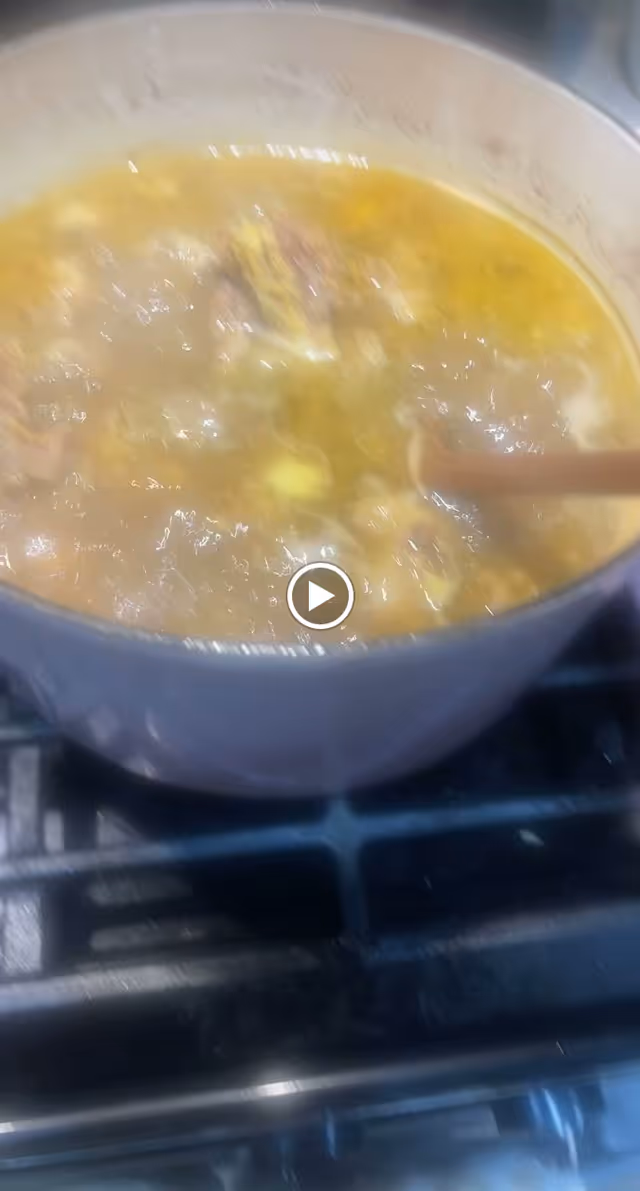 A pot of soup or stew simmering on a stove with a wooden spoon stirring the contents.