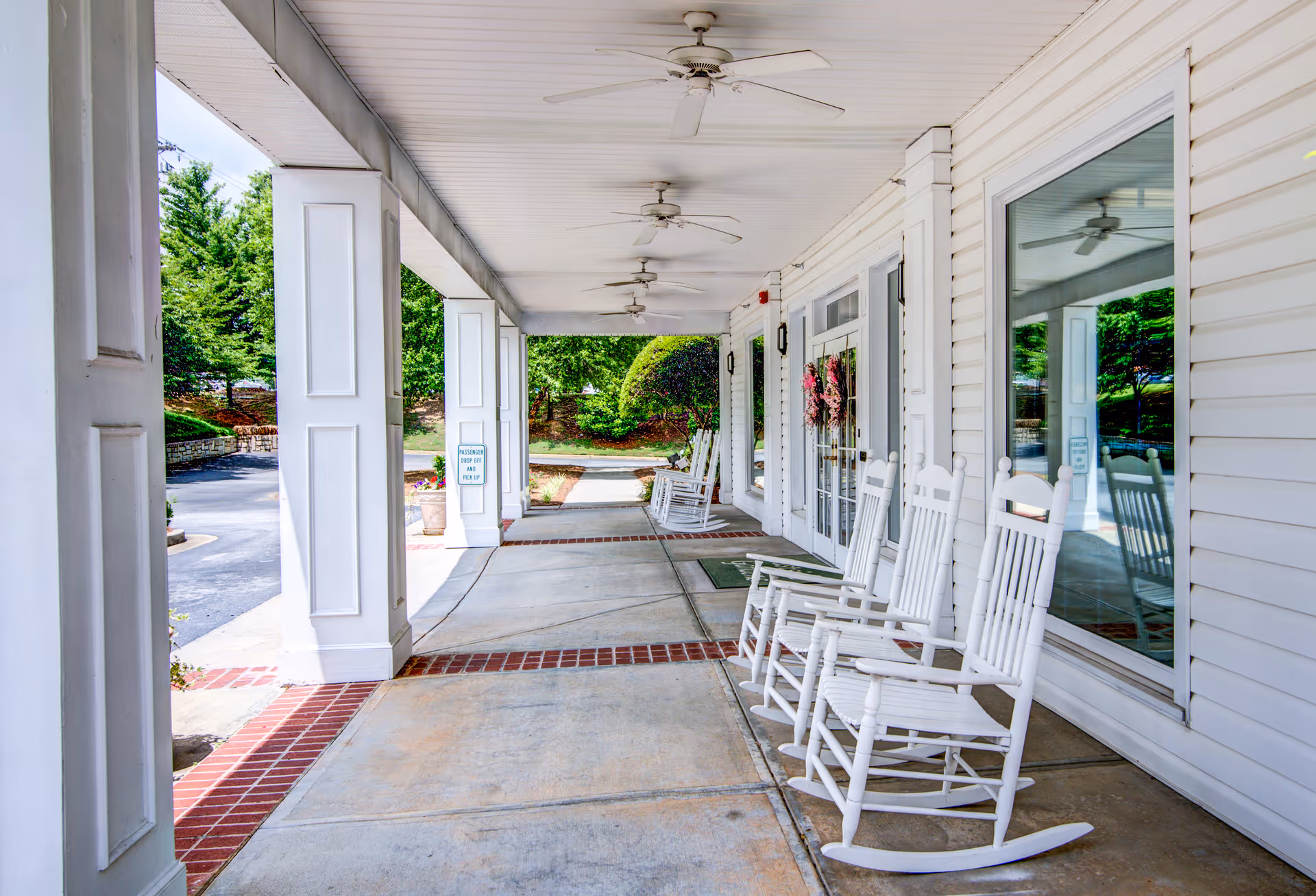 Covered front porch with white rocking chairs and ceiling fans along an entrance walkway.