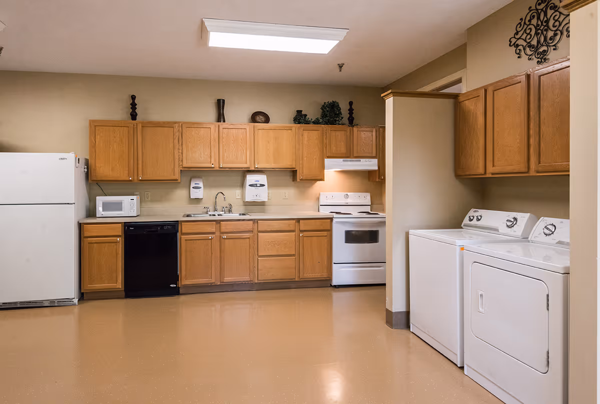 Communal kitchen and laundry area with wooden cabinets, refrigerator, stove, sink, dishwasher, and a washer and dryer.