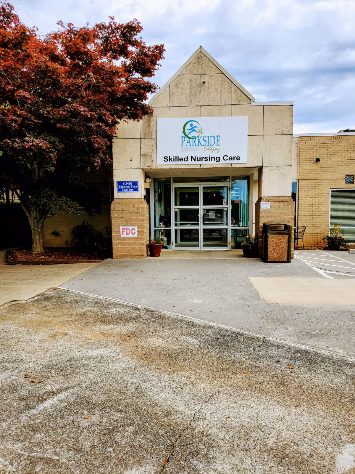 Front entrance of Parkside Skilled Nursing Care building with a sign above glass doors and a tree to the left.