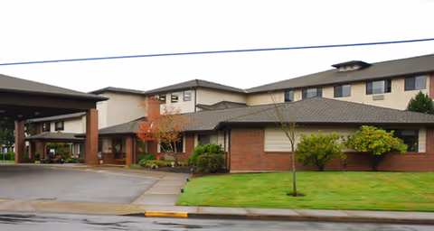 Exterior view of Brookdale McMinnville Town Center, a multi-story senior living facility with brick and beige siding, a covered entrance, and well-maintained green lawn and shrubs.