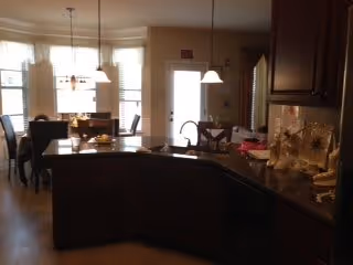 Open kitchen with a curved island and sink overlooking a dining area with a table and hanging lights.