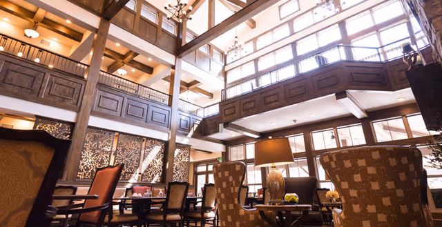 A spacious lobby with high ceilings, large windows, and wooden beams. Comfortable seating areas with stylish chairs and tables are arranged throughout, creating a welcoming atmosphere.