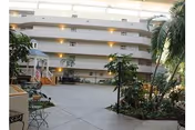 Large multi-story indoor atrium with potted plants, seating areas, and balcony-lined walkways.