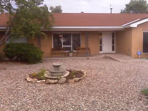Front view of a senior living facility entrance with a gravel courtyard fountain.