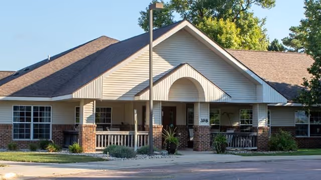 Front view of a single-story residential-style building with a covered porch, brick columns, and a lamp post.