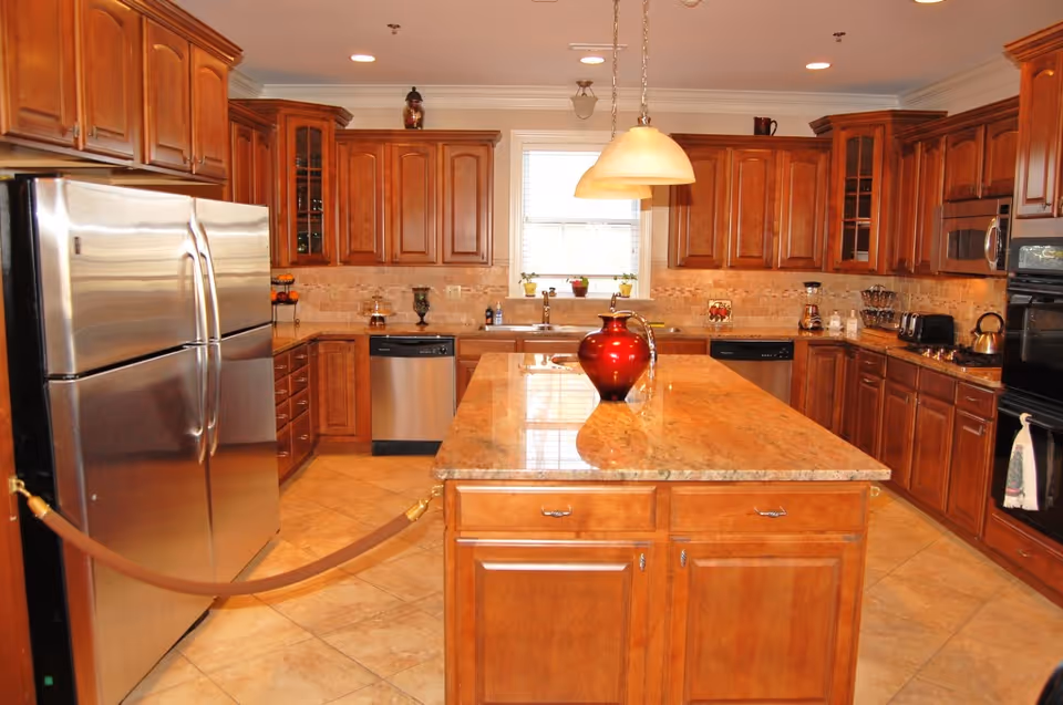 Spacious kitchen with wooden cabinets, a large central island topped with a red vase, stainless steel appliances and pendant lighting.