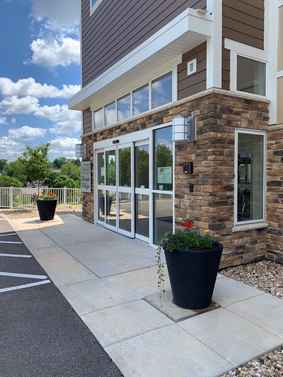 Entrance of New Glarus Home senior living facility featuring stone and wood design with flower pots.