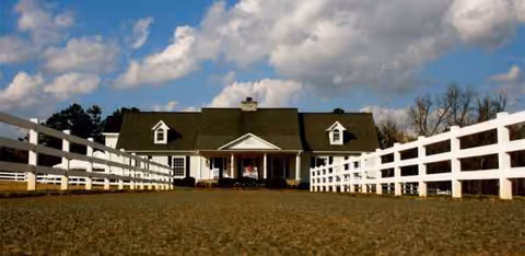 Gravel driveway leads to a white house-style facility flanked by fences.