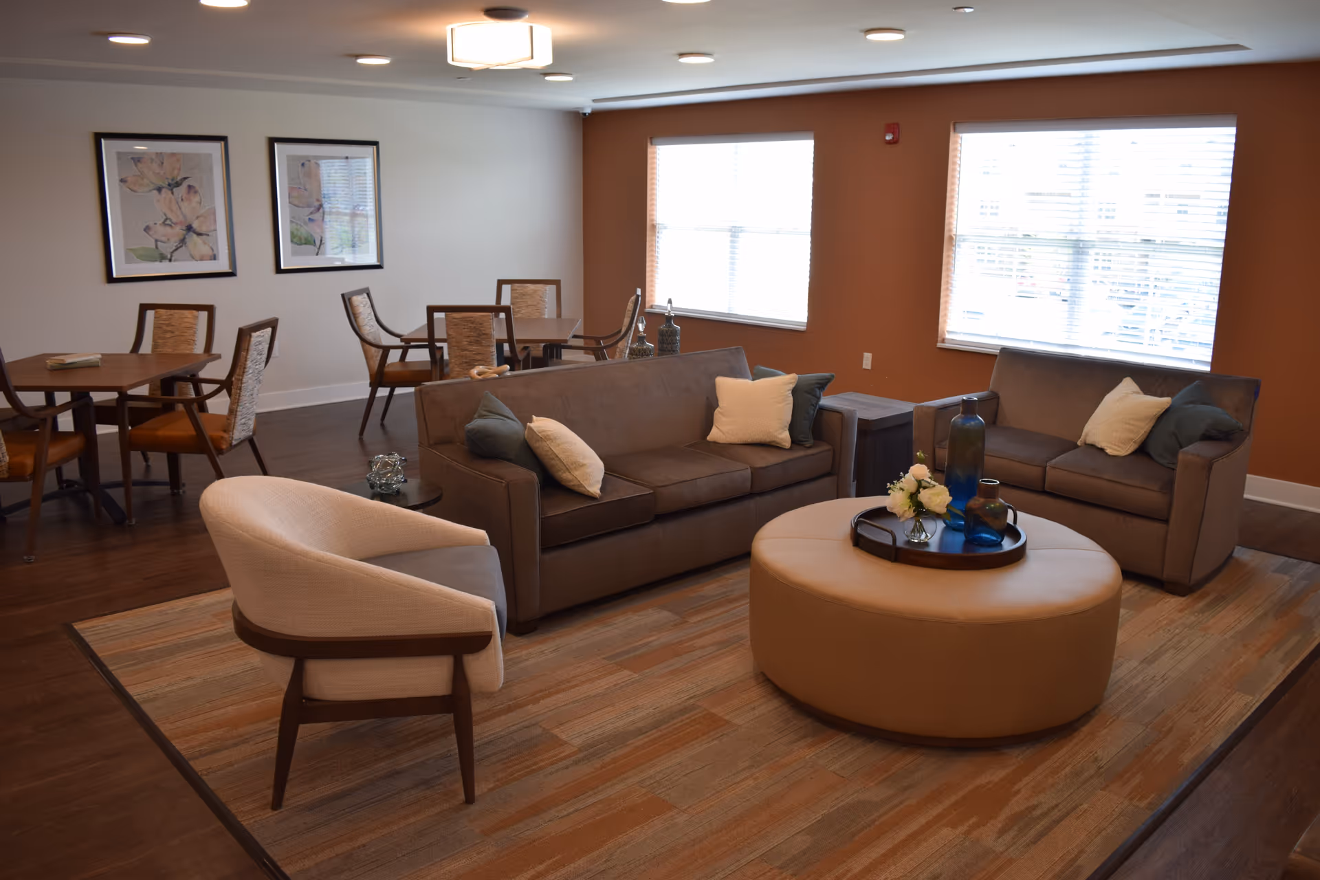Comfortable common living area with sofas, armchairs, a round ottoman and dining tables in the background.