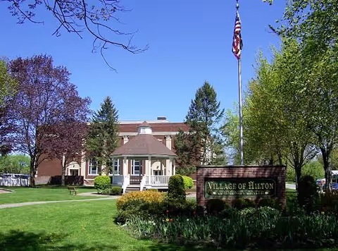 Exterior view of Hilton East Assisted Living building with manicured lawn and flagpole.