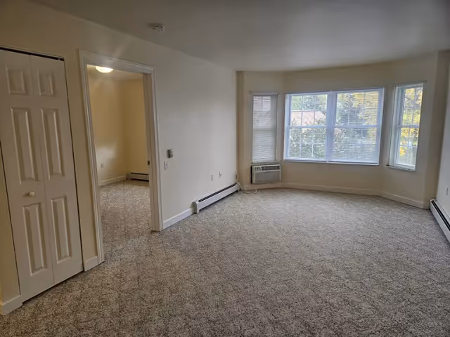 Empty carpeted living room in Prairie View Senior Living with bay windows.