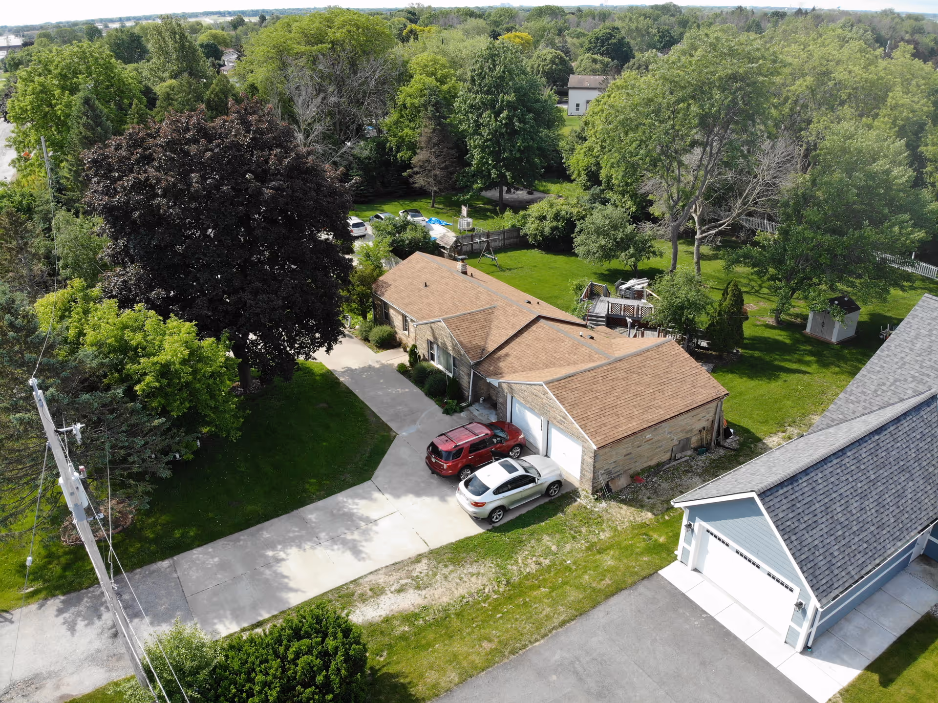 Aerial view of a single-story residential building with a driveway, two parked cars, and surrounding trees and yard.