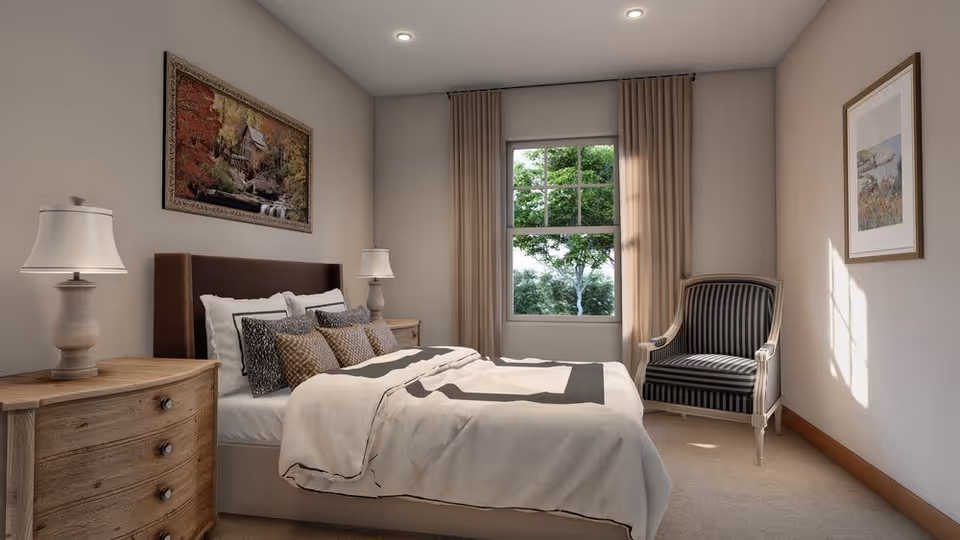 Sunlit bedroom with a made bed, two bedside tables with lamps, a striped armchair by a window showing trees, and framed art on the walls.