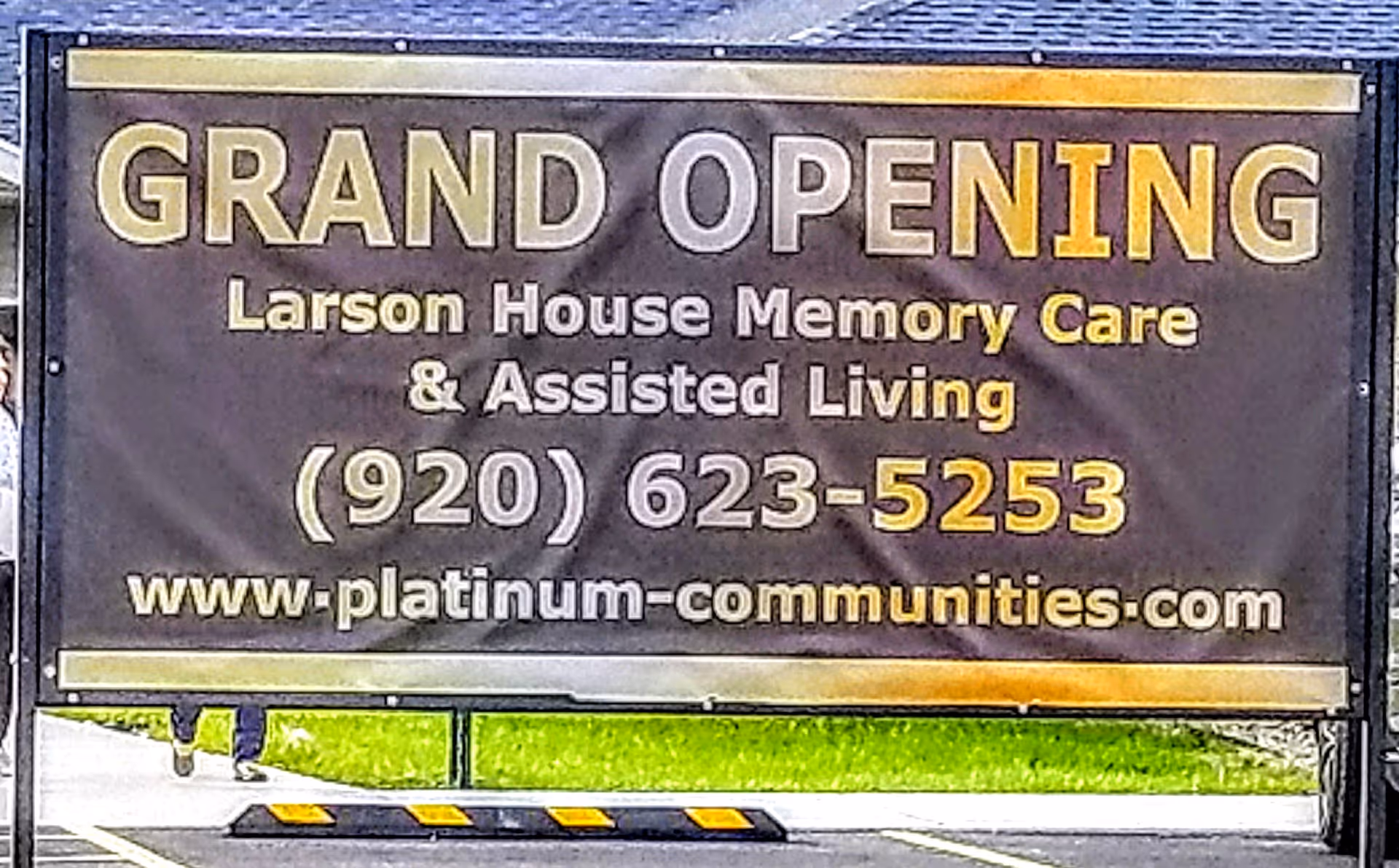 A large outdoor banner announcing the grand opening of Larson House Memory Care & Assisted Living with a phone number and website.