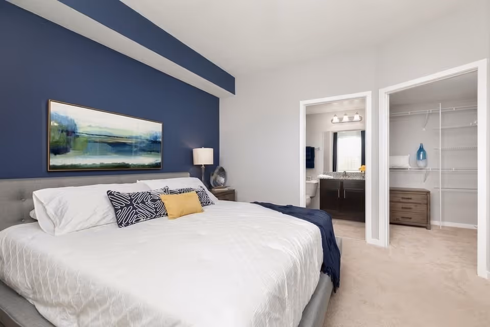 Bright modern bedroom with a large bed, navy accent wall, and open doorways to a bathroom and walk-in closet.