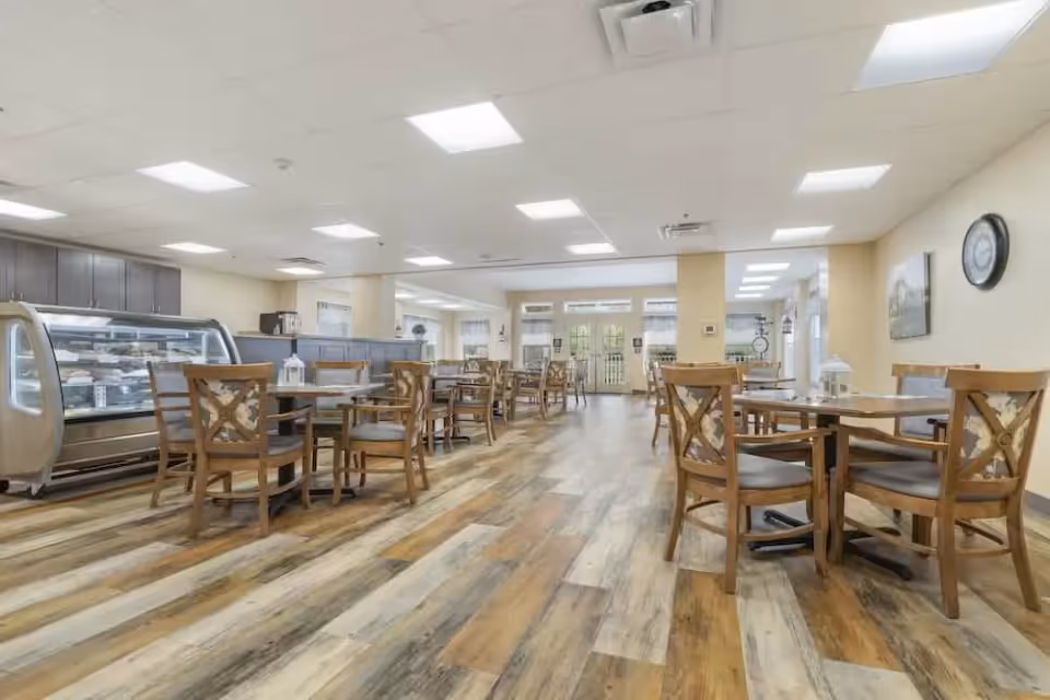 Spacious dining room with wooden tables and chairs, a glass display case on the left, and bright overhead lighting.