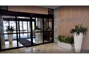 Entrance lobby with glass automatic sliding doors, potted plants and a wood-paneled wall reading 'PENINSULA'.