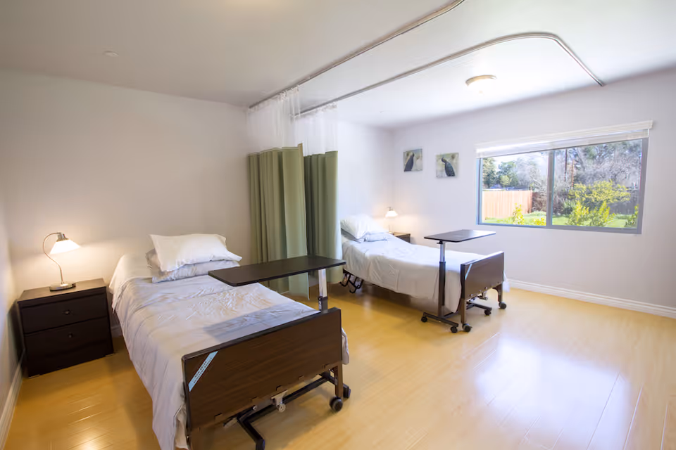 A bright and spacious shared bedroom with two adjustable beds and a window overlooking greenery.