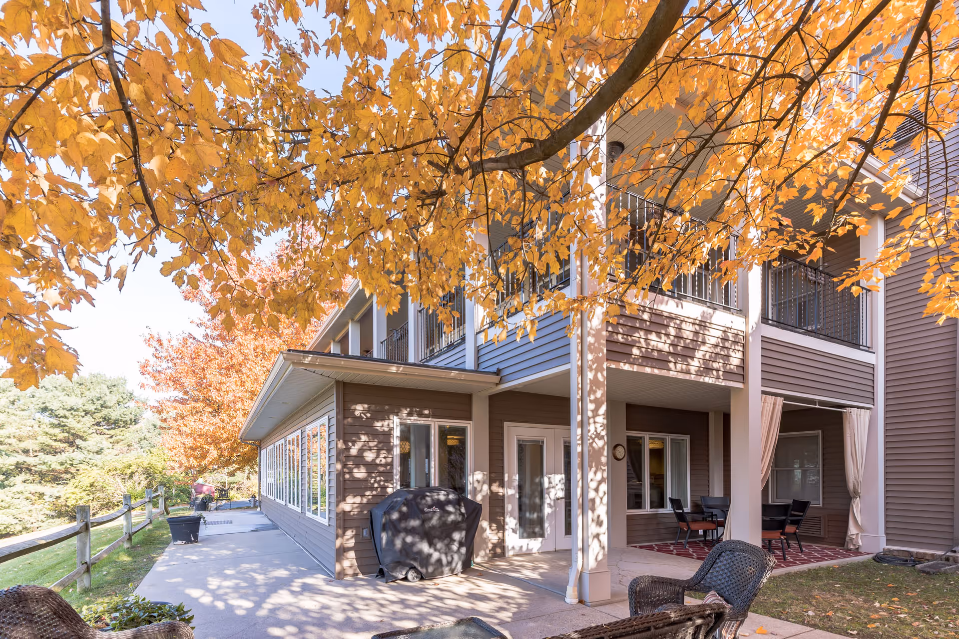 Covered patio and walkway of a senior living building framed by trees with bright orange autumn leaves.