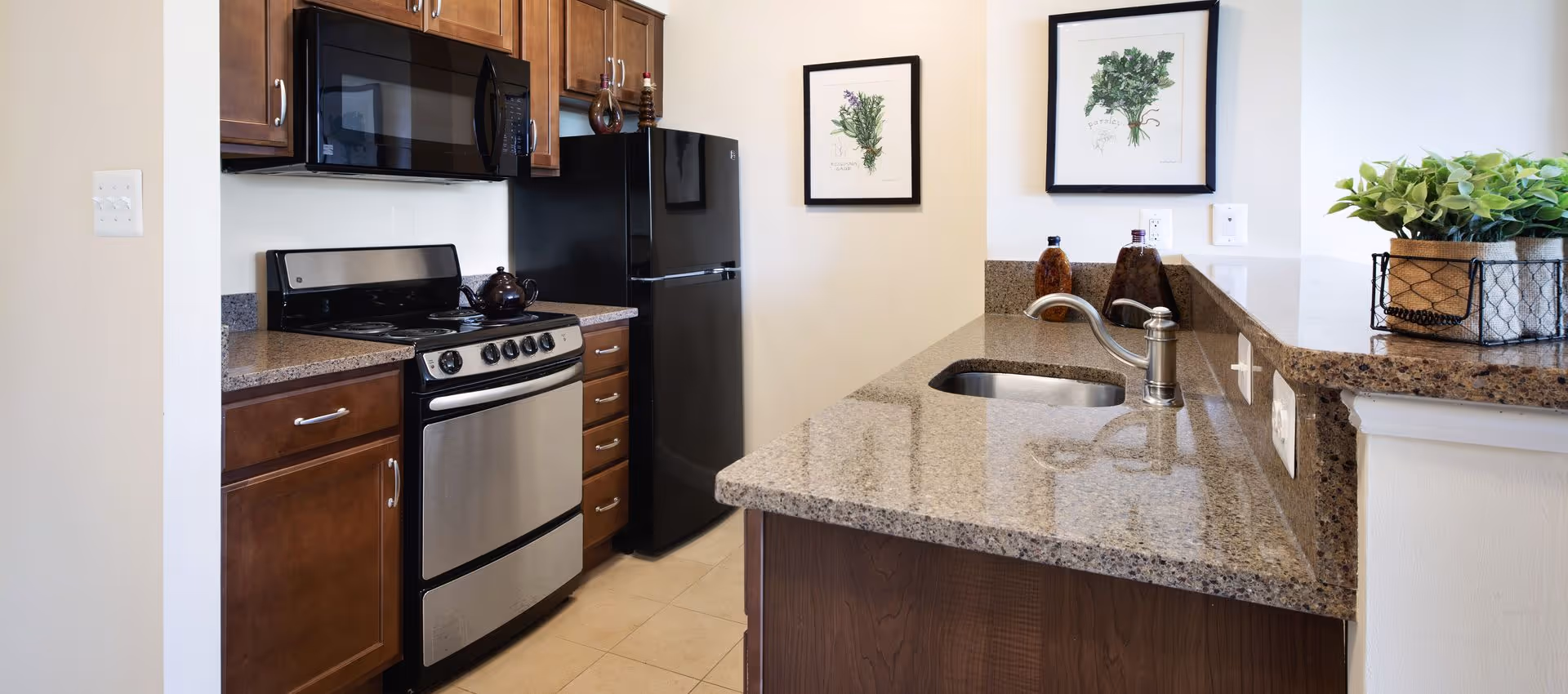 Small modern kitchen with granite countertops, a sink, stainless steel stove and microwave, black refrigerator, and wooden cabinets.