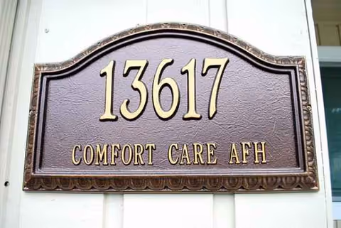 Exterior sign plaque displaying 13617 Comfort Care AFH on a light wall.