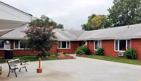 Exterior view of a red brick care center with benches, trees, and a paved courtyard.
