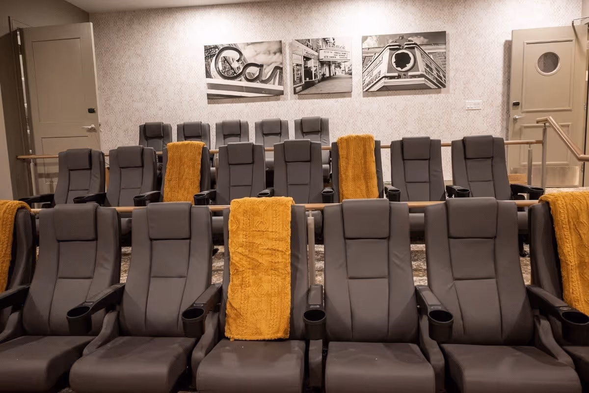 Rows of gray reclining theater seats with yellow throws in a small screening room with black-and-white wall art on the back wall.