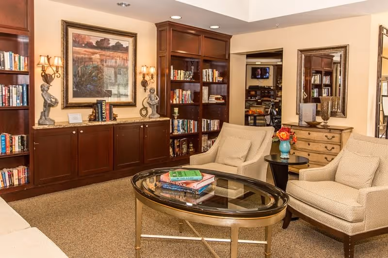 Cozy communal living room with two armchairs, a glass-top coffee table with books, built-in bookshelves, and decorative artwork.