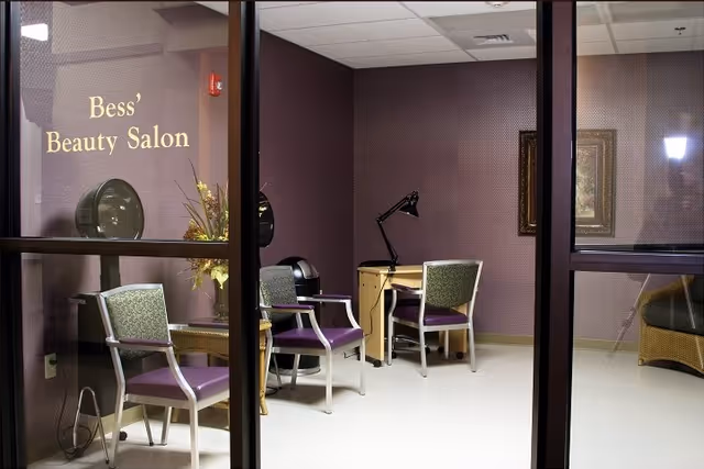 Interior view of Bess' Beauty Salon showing salon chairs, hair dryers, a desk with a lamp, and a wall sign reading "Bess' Beauty Salon".