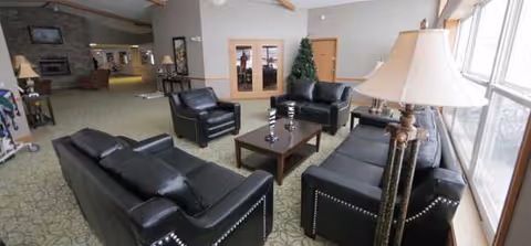 A spacious senior living lounge with black leather seating, a coffee table, and large windows.