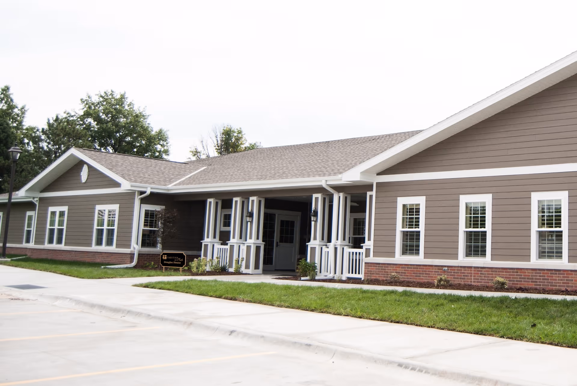 Single-story brown-and-white building with a covered main entrance, multiple windows, a small lawn, and a parking area.