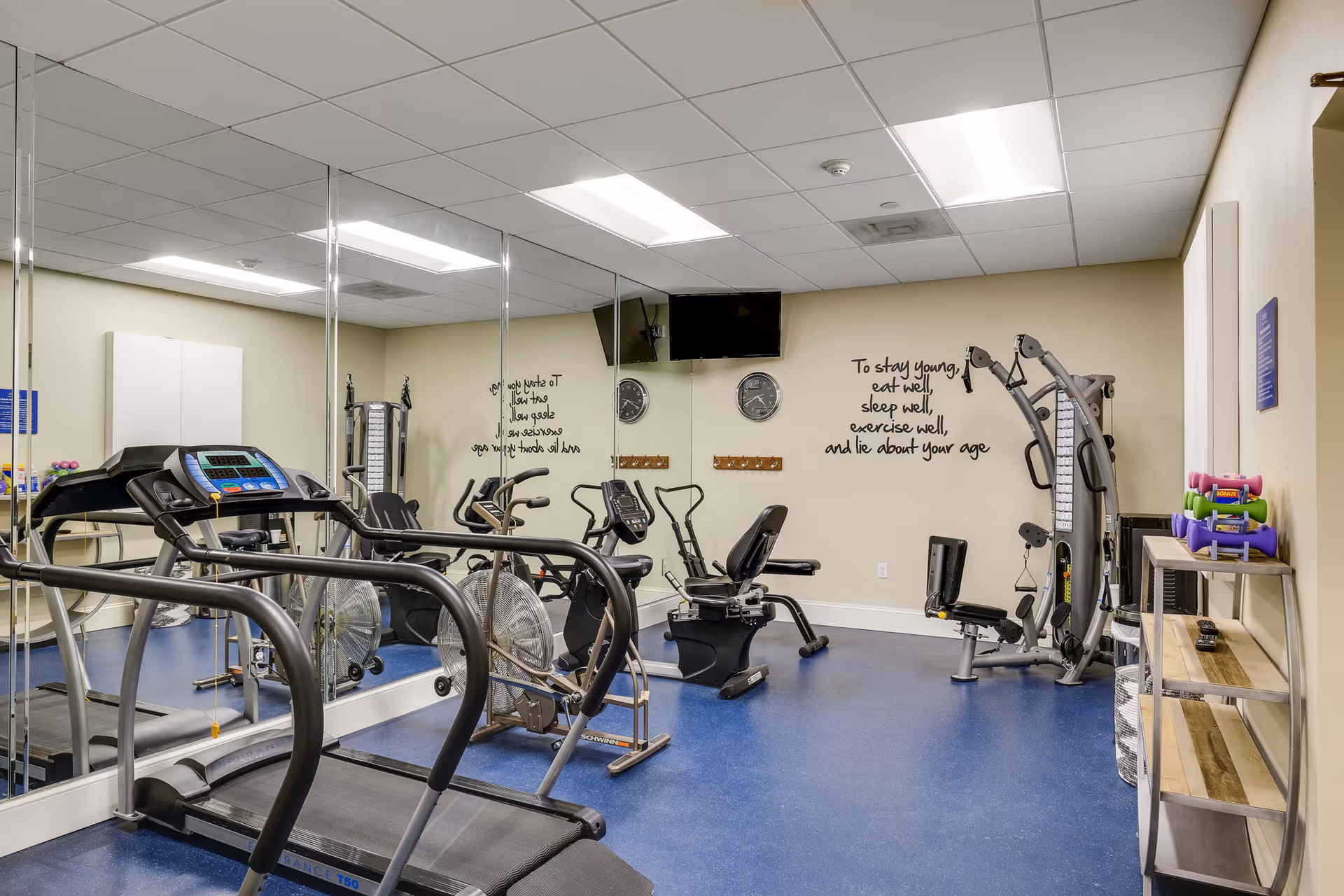 Fitness room with treadmills, stationary bikes, a multi‑station weight machine, mirrored wall and motivational wall text.