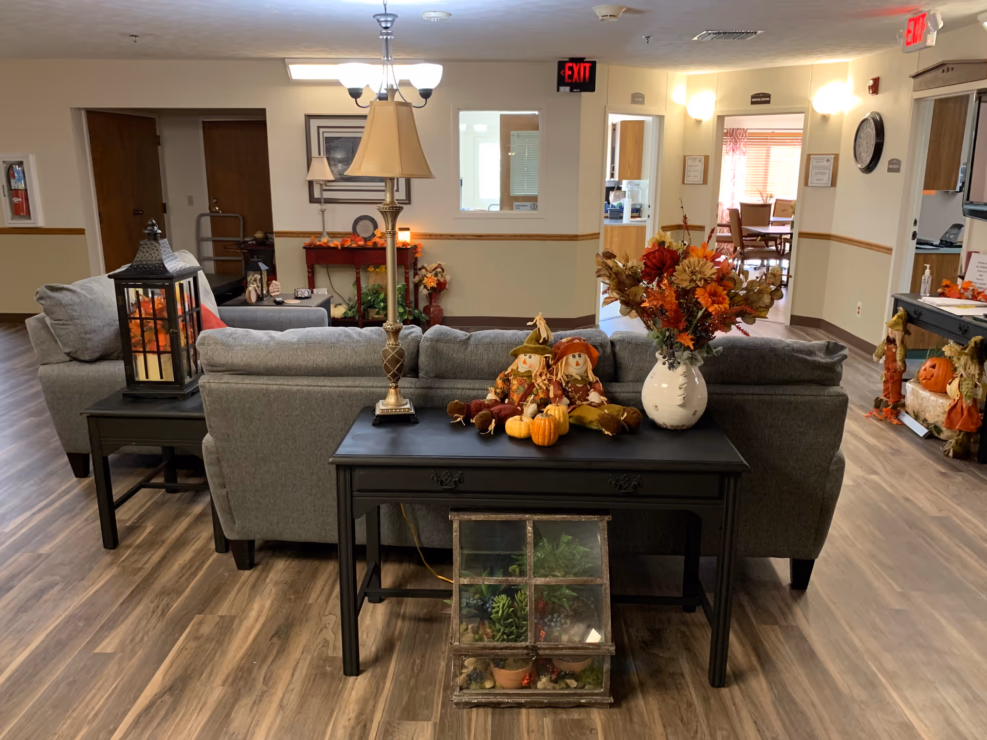 Communal lounge area with gray sofas, side tables and autumn decorations in a retirement community common room.
