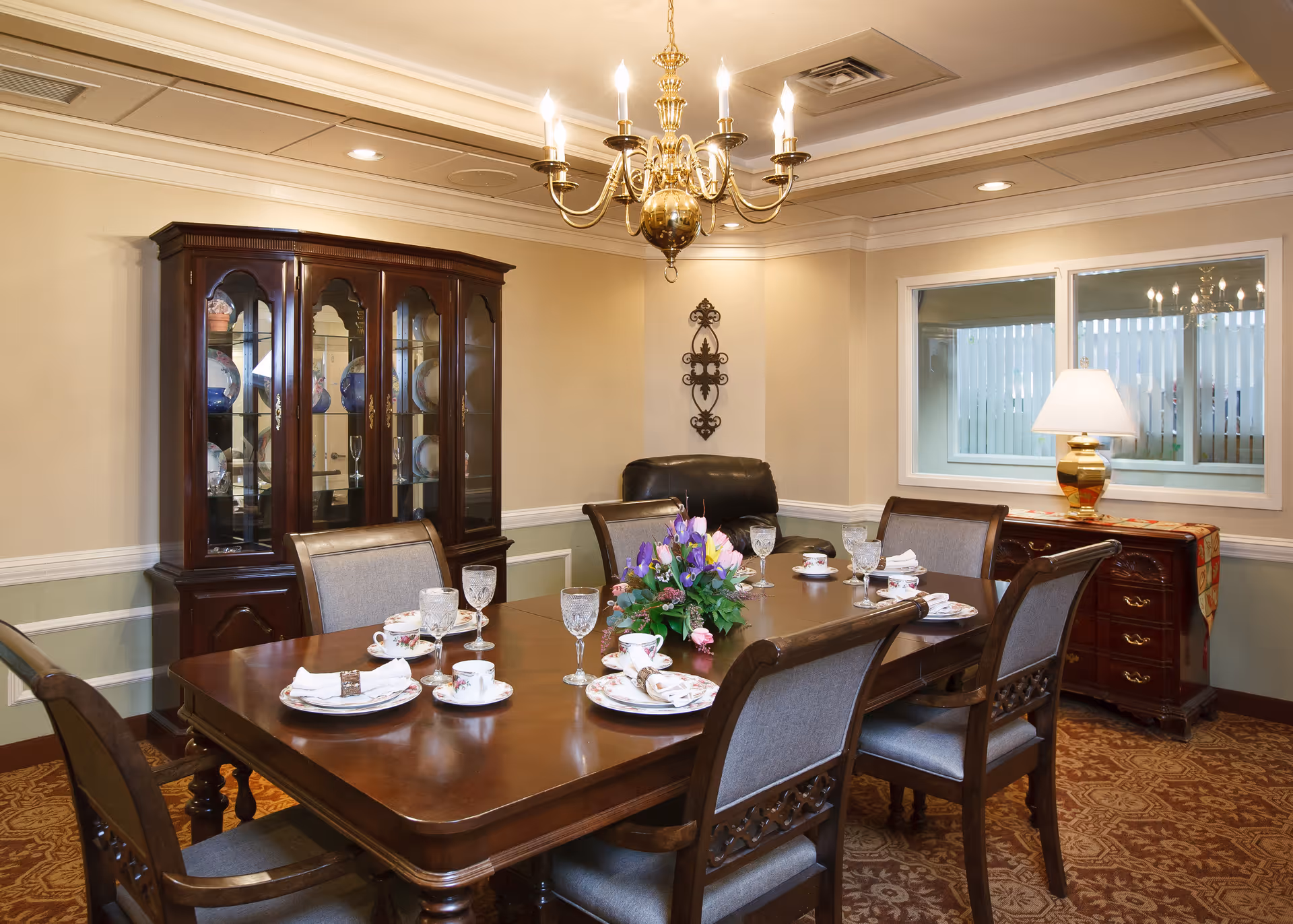 Formal dining room with a wooden table set with china and glassware, a chandelier overhead, a china cabinet and sideboard.