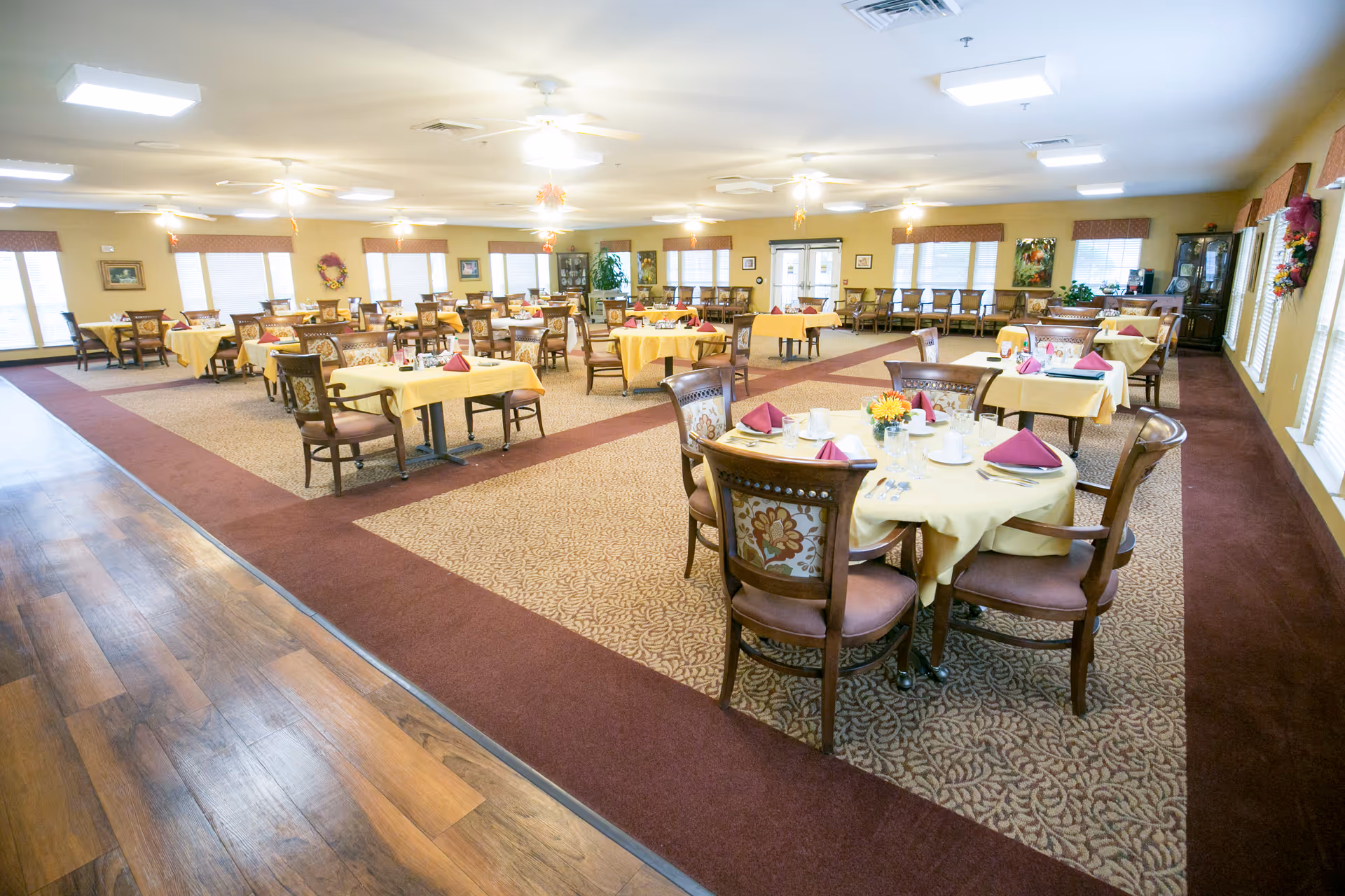 Spacious dining room with multiple round and rectangular tables set with yellow tablecloths and folded napkins.