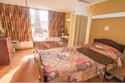 Shared senior living bedroom with two beds, curtains, window, and privacy divider.