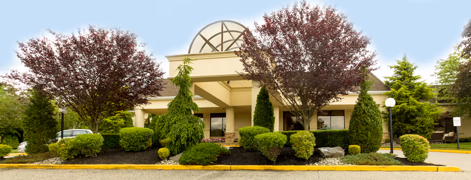 Front view of a senior care facility with landscaped shrubs, trees, and a rounded glass dome.