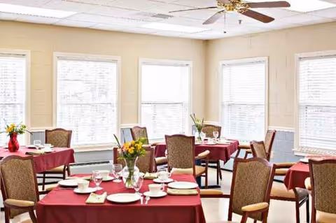 Bright dining room with maroon tablecloths, place settings, and arranged chairs near windows.