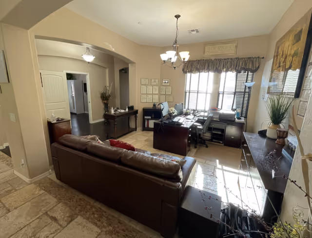 Sunlit living room and home office with a leather sofa, a desk under windows, and decorative furnishings.